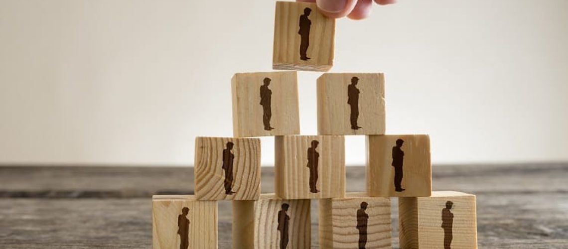 Man stacking a tower of wood blocks with human silhouettes, human resources and management concept.